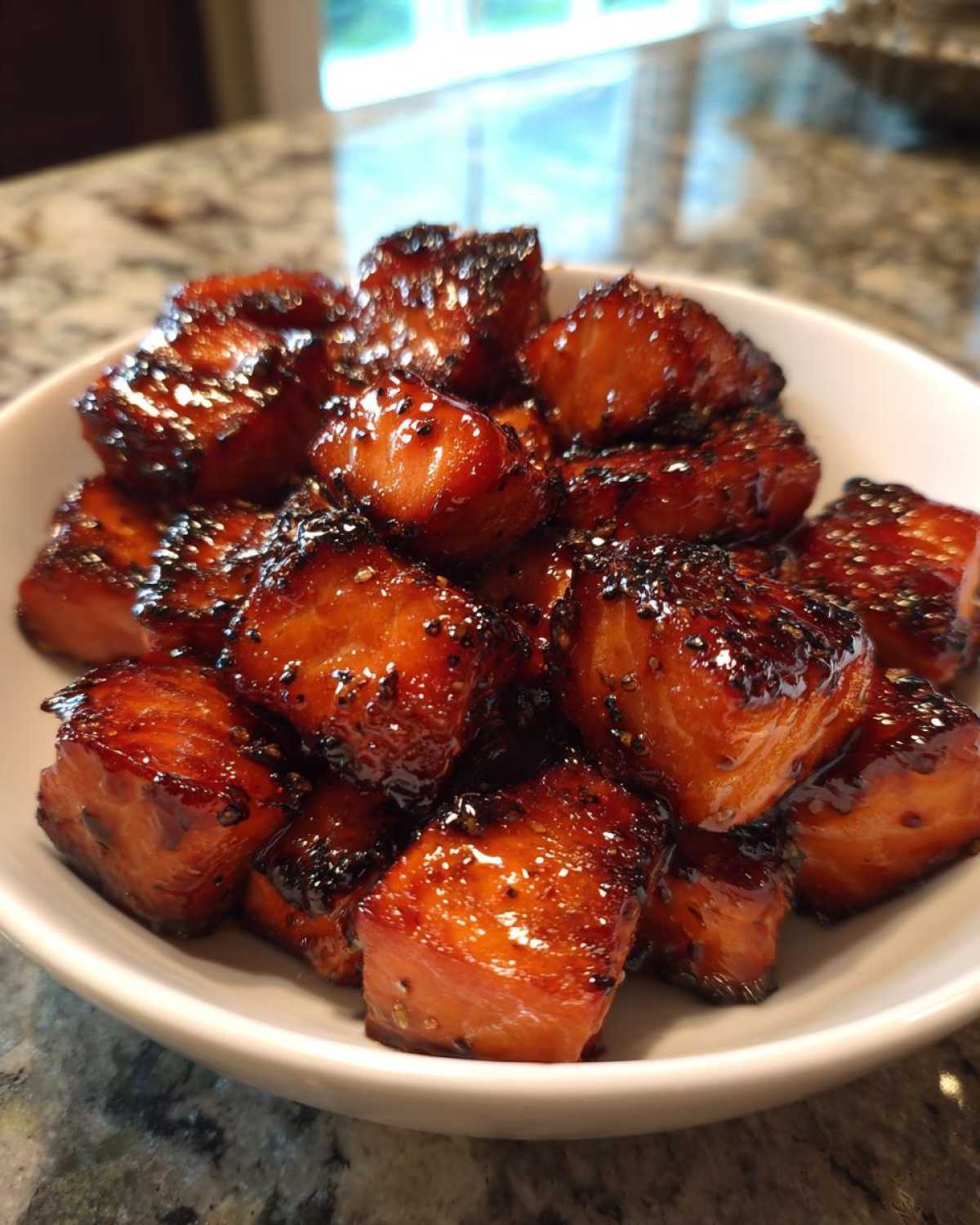 Close-up of glistening Honey Garlic Salmon Bites with caramelized edges piled high in a white serving bowl.