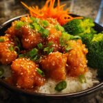 Close-up of a Honey Sriracha Chicken Bowl featuring glazed chicken pieces over rice with broccoli and sesame seeds.
