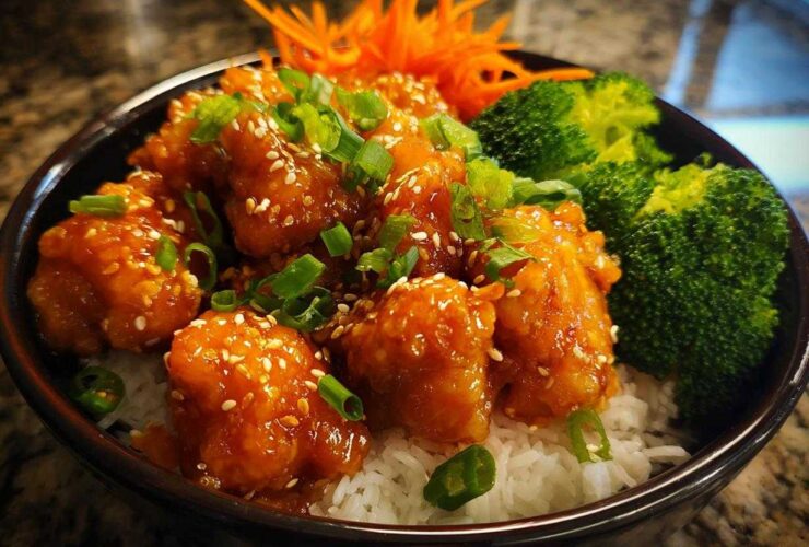 Close-up of a Honey Sriracha Chicken Bowl featuring glazed chicken pieces over rice with broccoli and sesame seeds.