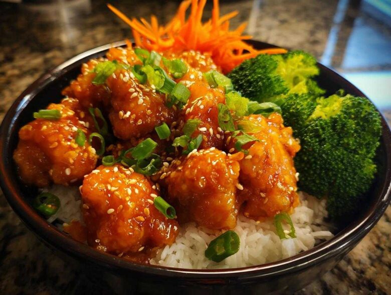 Close-up of a Honey Sriracha Chicken Bowl featuring glazed chicken pieces over rice with broccoli and sesame seeds.