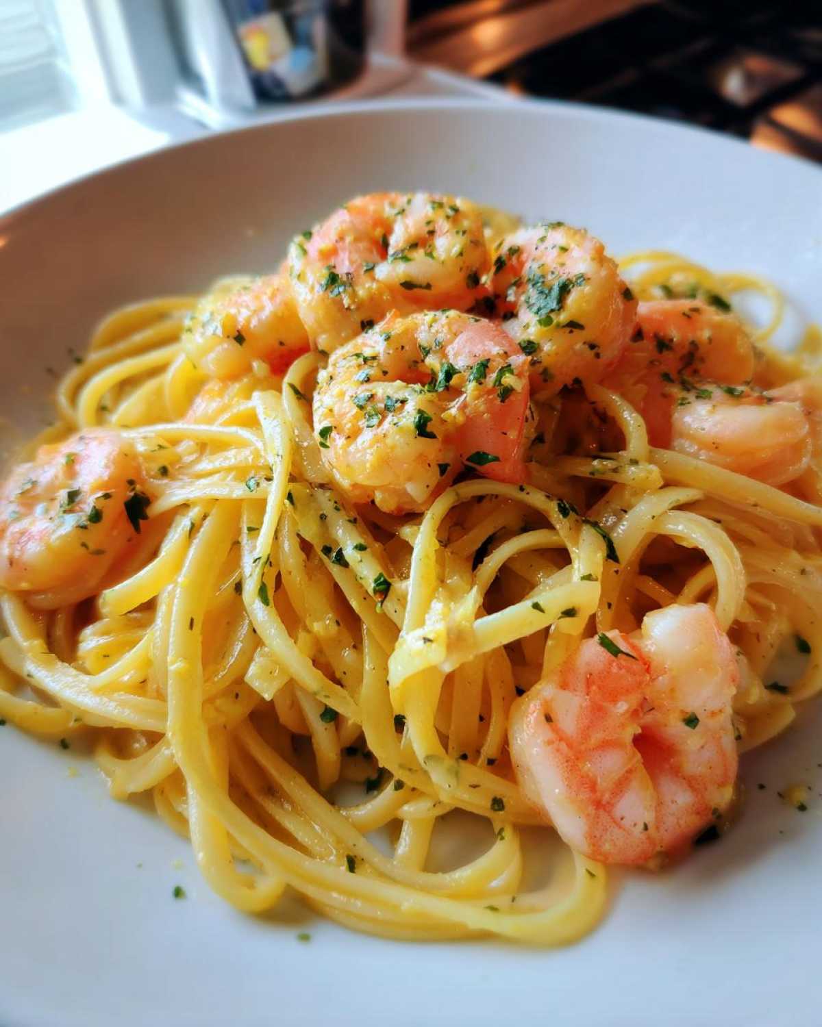 A close-up of a white bowl filled with Lemon Butter Shrimp Pasta, featuring linguine coated in a rich sauce and topped with pink shrimp and parsley.