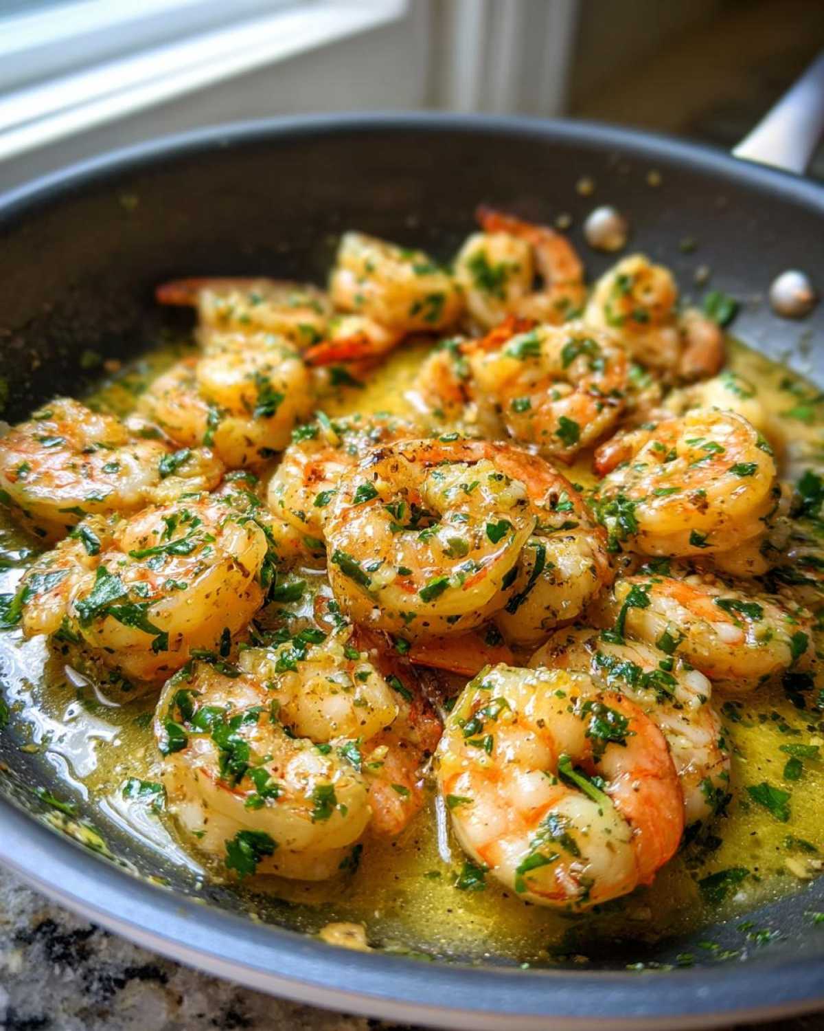 Close-up of plump shrimp sizzling in a skillet with rich lemon garlic butter sauce and fresh parsley.