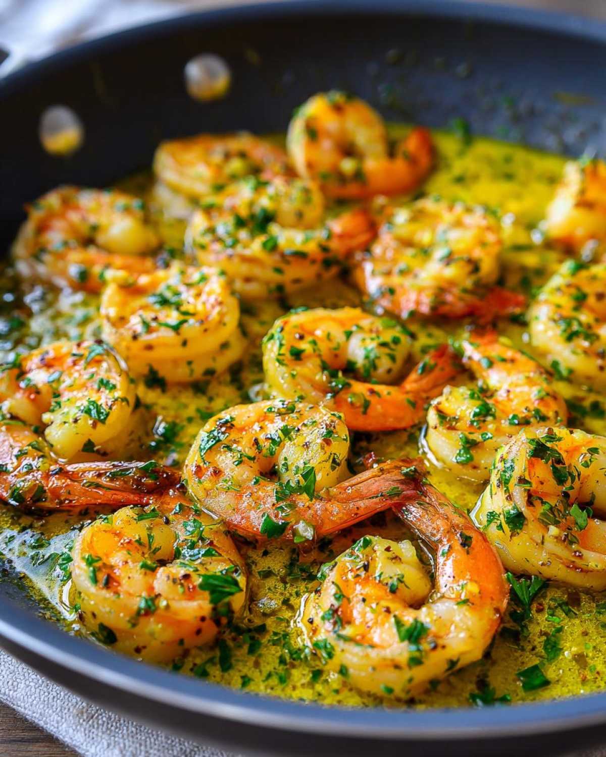 Close-up of plump shrimp sizzling in a pan with bright lemon garlic butter sauce and fresh parsley.