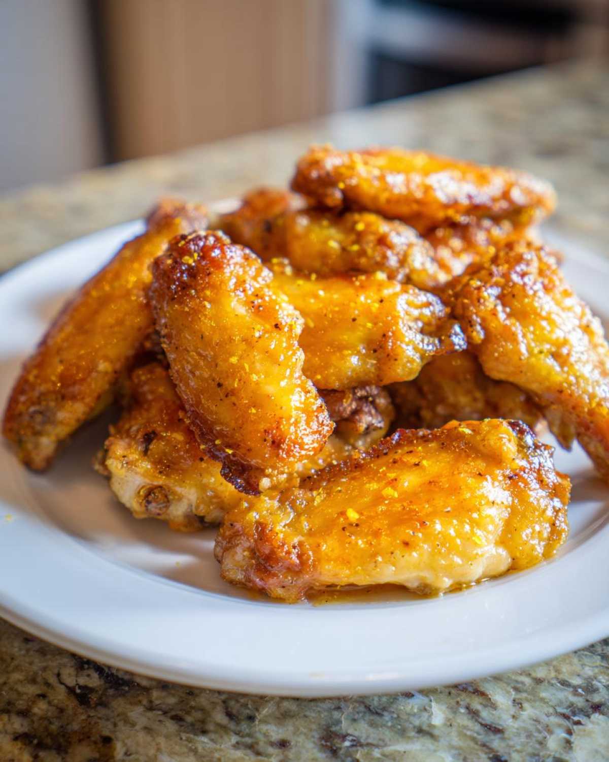 A close-up of a pile of golden, crispy Lemon Pepper Chicken Wings Oven Style seasoned with visible lemon zest, served on a white plate.