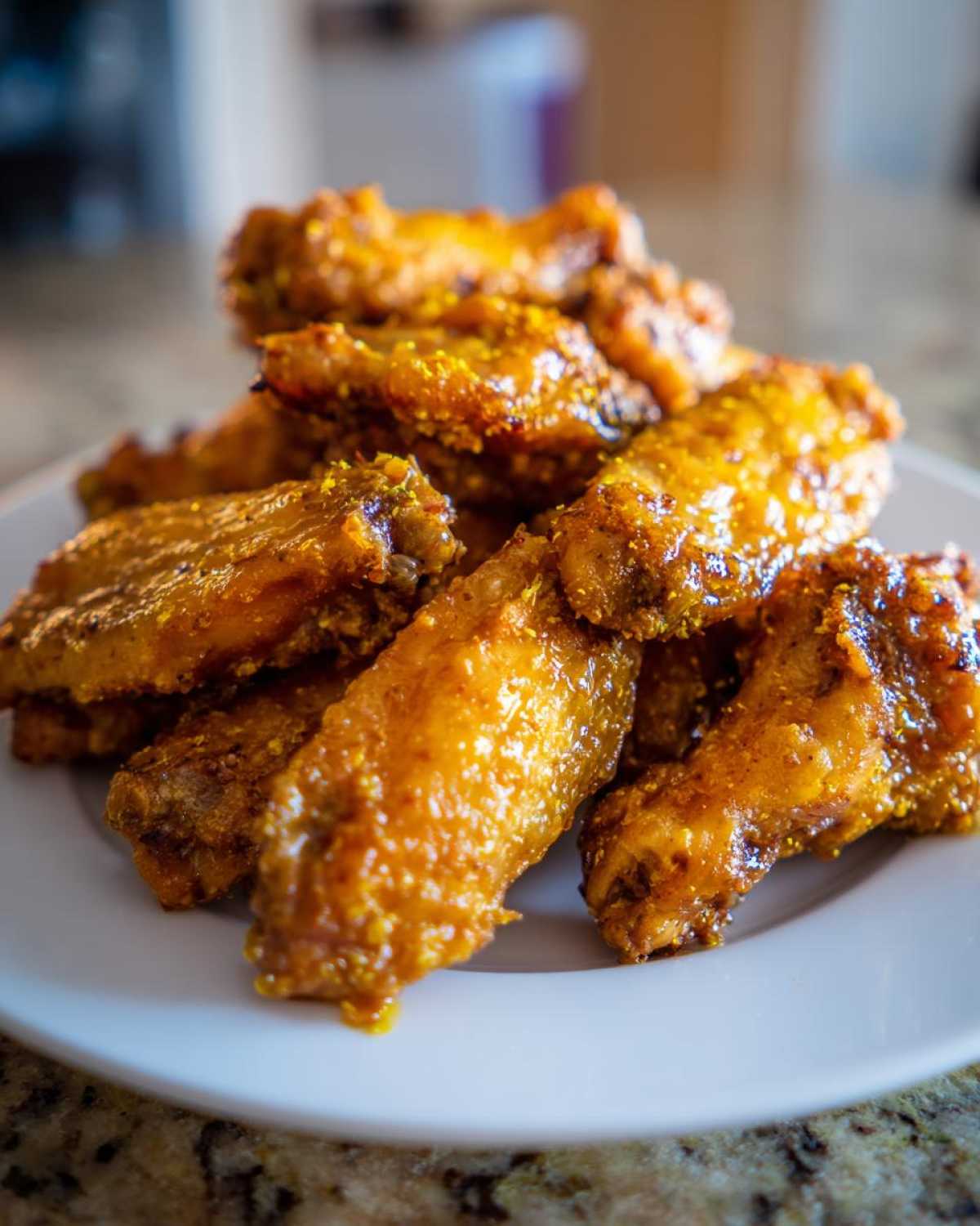 A pile of golden, crispy Lemon Pepper Chicken Wings Oven Style glistening with sauce on a white plate.