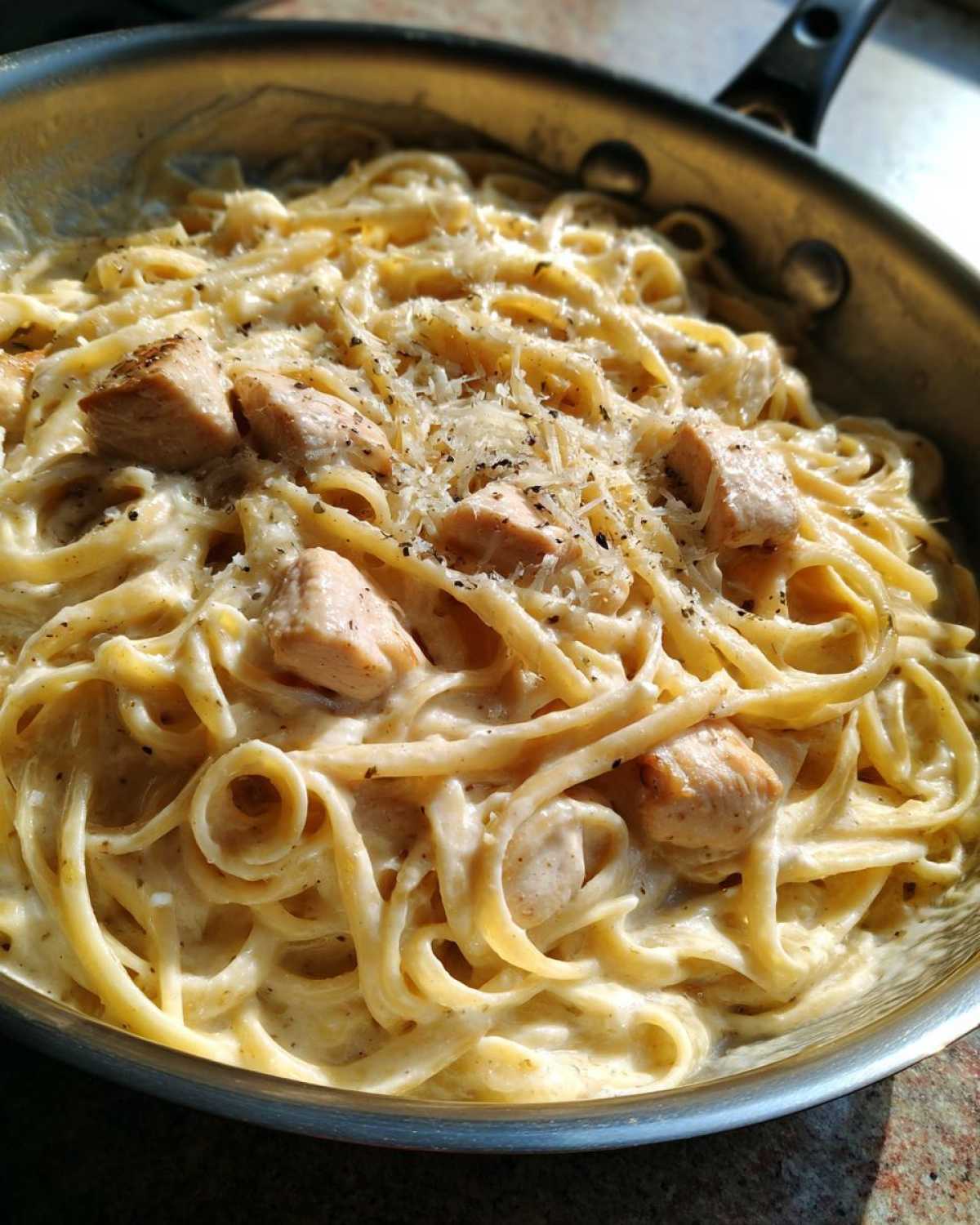 Close-up of rich, creamy Alfredo pasta with chunks of chicken, topped with grated cheese and black pepper.