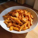 A close-up of a white bowl filled with One Pot Creamy Tomato Pasta with Chicken, topped with chili flakes.