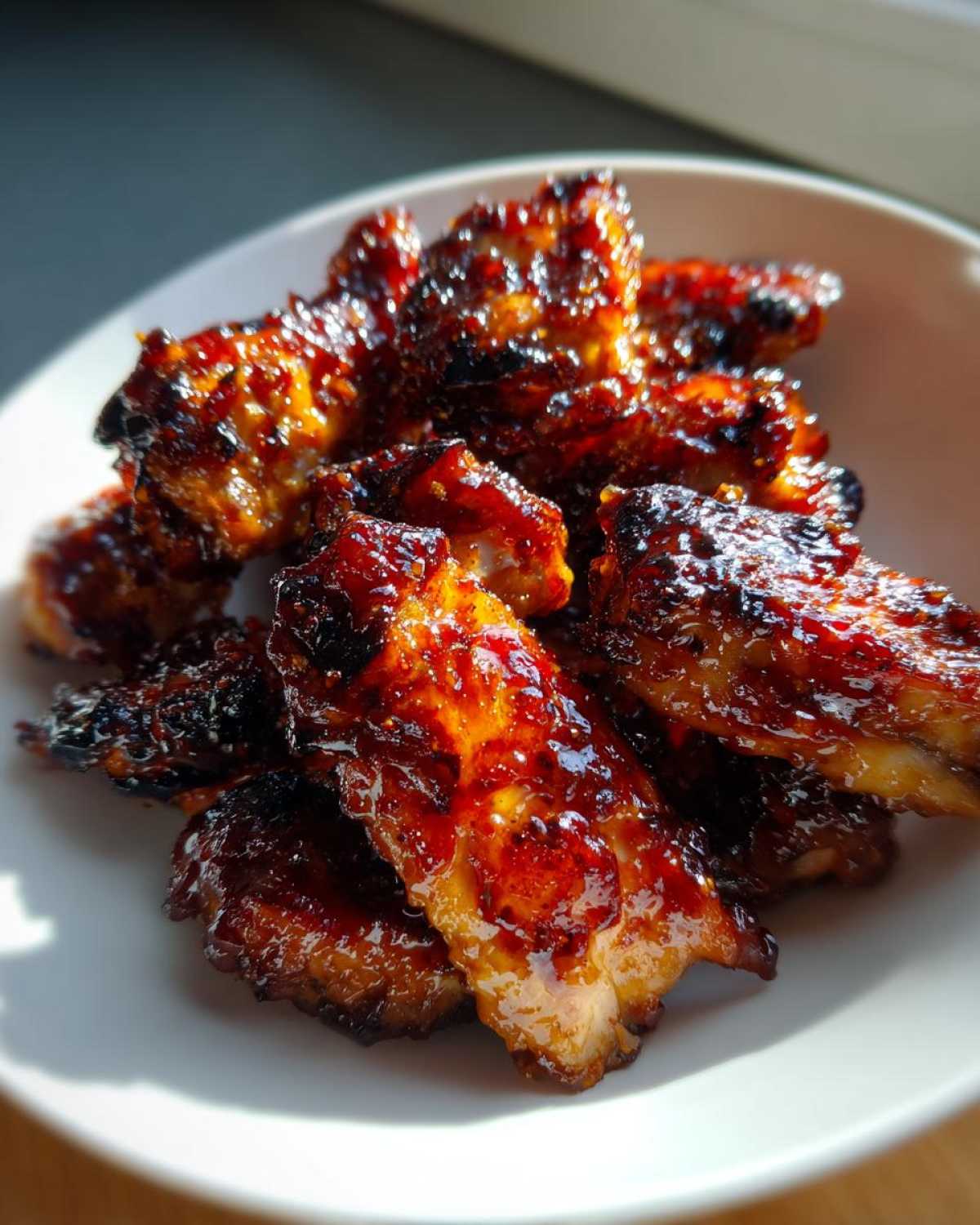 Close-up of glistening, caramelized Sticky BBQ Chicken Bites piled high in a white bowl, catching the sunlight.
