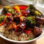 A close-up of a Sticky BBQ Chicken Bowl with Veggies served over brown rice, glistening with sauce.