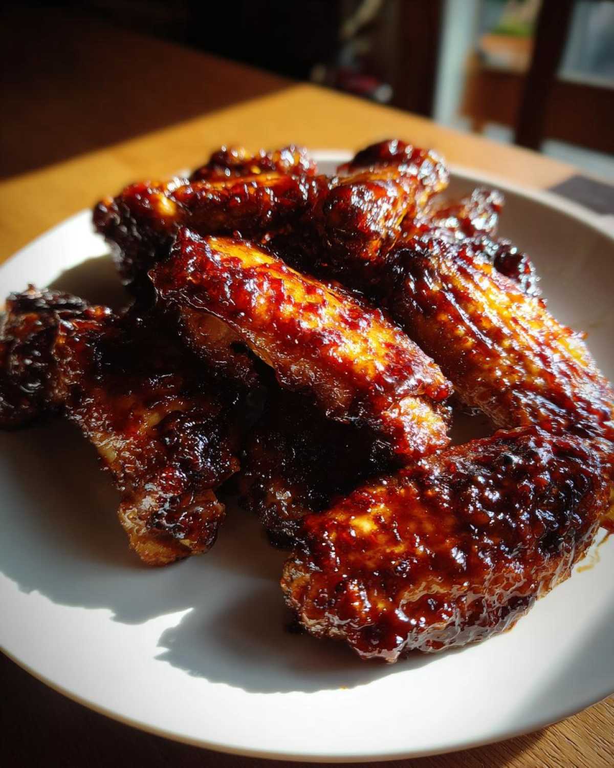 A pile of glistening, caramelized Sticky BBQ Chicken Wings with Honey Glaze served on a white plate.
