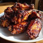 A pile of perfectly cooked Sticky BBQ Chicken Wings with Honey Glaze, glistening under bright light.