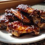 Close-up of sticky, glazed Honey Garlic Chicken Wings Oven Baked piled on a white plate.