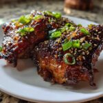 Close-up of two Sticky Honey Soy Chicken Thighs with Garlic, coated in a dark, glossy sauce and topped with sesame seeds and green onions.
