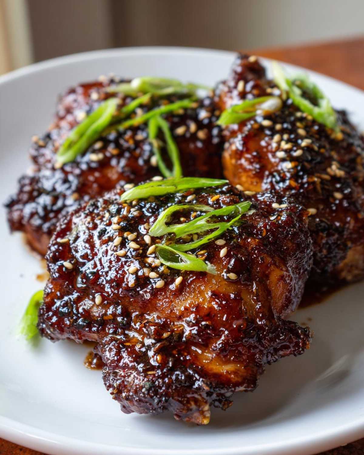 Close-up of Sticky Honey Soy Chicken Thighs with Garlic, coated in a dark glaze and topped with sesame seeds and green onions.
