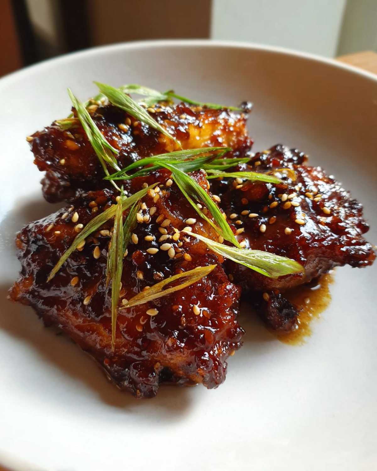 Close-up of three pieces of Sticky Honey Soy Chicken Thighs with Garlic, coated in a dark, glossy glaze and topped with sesame seeds and scallions.