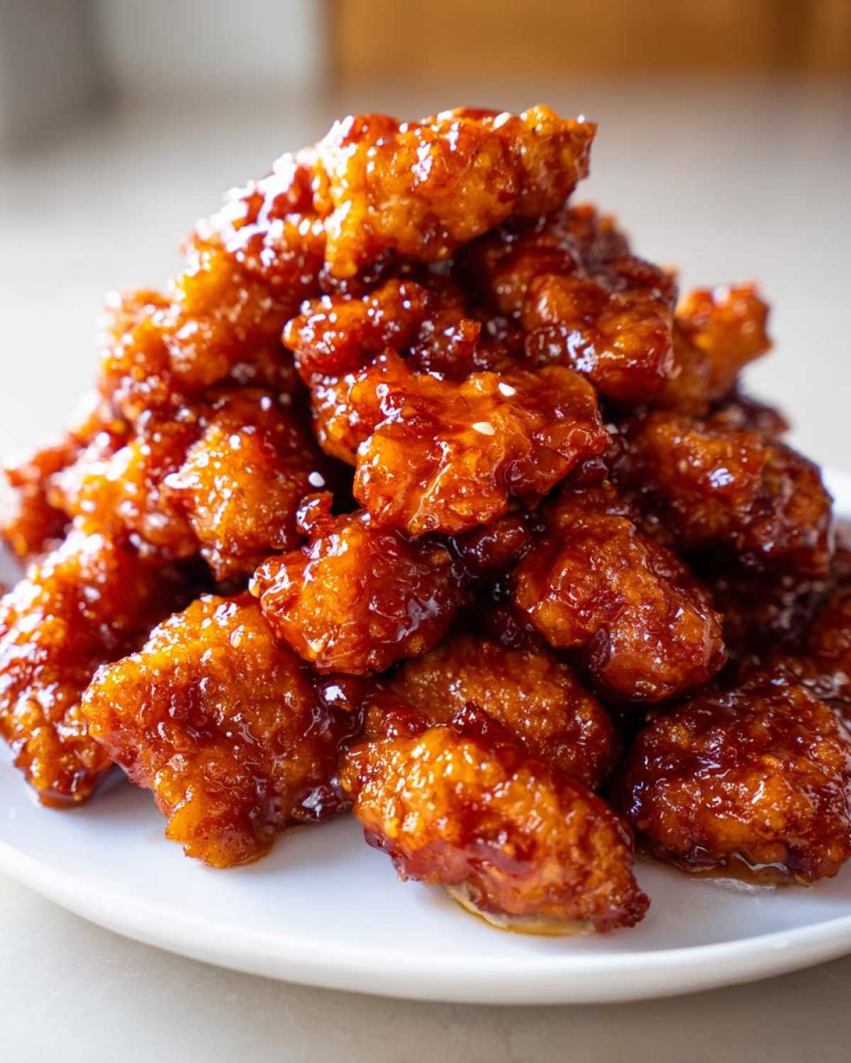 A close-up, mouthwatering pile of crispy, glazed Sticky Orange Chicken Better Than Takeout on a white plate.