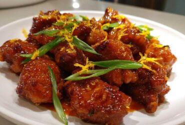 Close-up of glazed Sticky Orange Chicken Thighs topped with bright orange zest and green scallions.