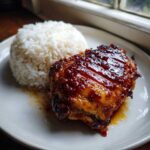 Close-up of Sticky Sweet Chili Chicken Thighs glazed with a thick, shiny sauce next to a mound of white rice.