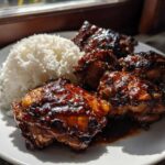 Four glazed Sticky Sweet Chili Chicken Thighs served next to a mound of fluffy white rice on a white plate.
