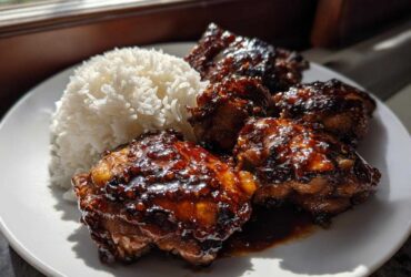 Four glazed Sticky Sweet Chili Chicken Thighs served next to a mound of fluffy white rice on a white plate.