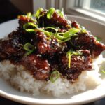 Close-up of Sticky Sweet Soy Chicken with Rice, glazed dark brown and topped with green onions and sesame seeds.