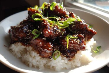 Close-up of Sticky Sweet Soy Chicken with Rice, glazed dark brown and topped with green onions and sesame seeds.