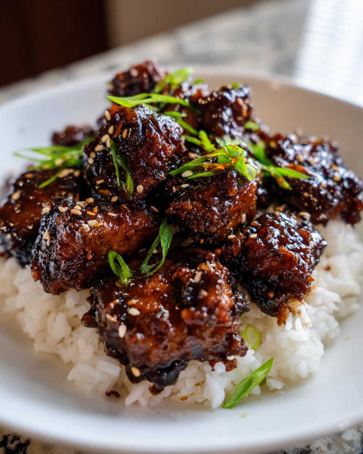 Close-up of Sticky Teriyaki Chicken Bites coated in a dark, glossy sauce, served over a bed of white rice and garnished with sesame seeds and green onions.