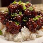 Close-up of glossy Sticky Teriyaki Chicken Bites piled high on a bed of white rice, garnished with sesame seeds and green onions.