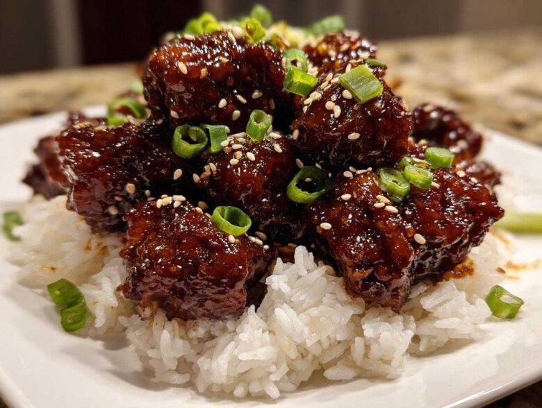 Close-up of glossy Sticky Teriyaki Chicken Bites piled high on a bed of white rice, garnished with sesame seeds and green onions.