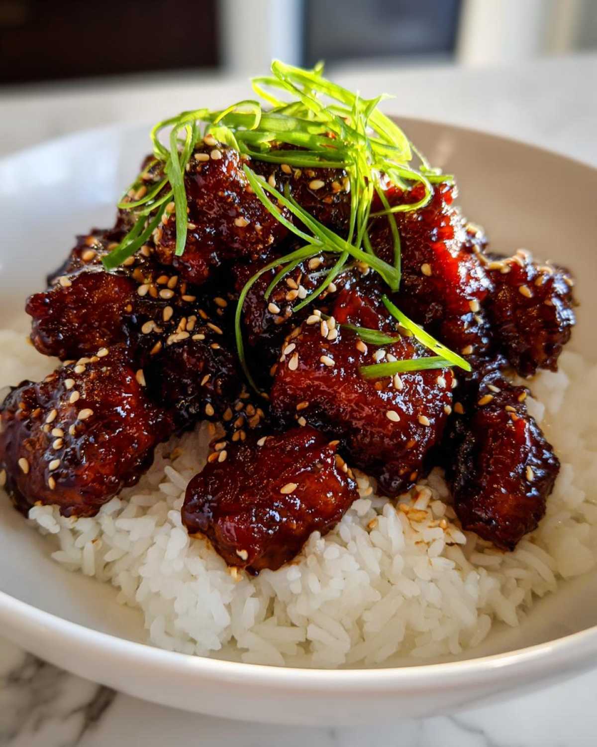 Close-up of Sticky Teriyaki Chicken Bites coated in dark glaze, sprinkled with sesame seeds, and topped with green onions over white rice.