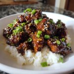 Close-up of Sticky Teriyaki Chicken Bites coated in dark glaze, served over fluffy white rice and topped with sesame seeds and green onions.