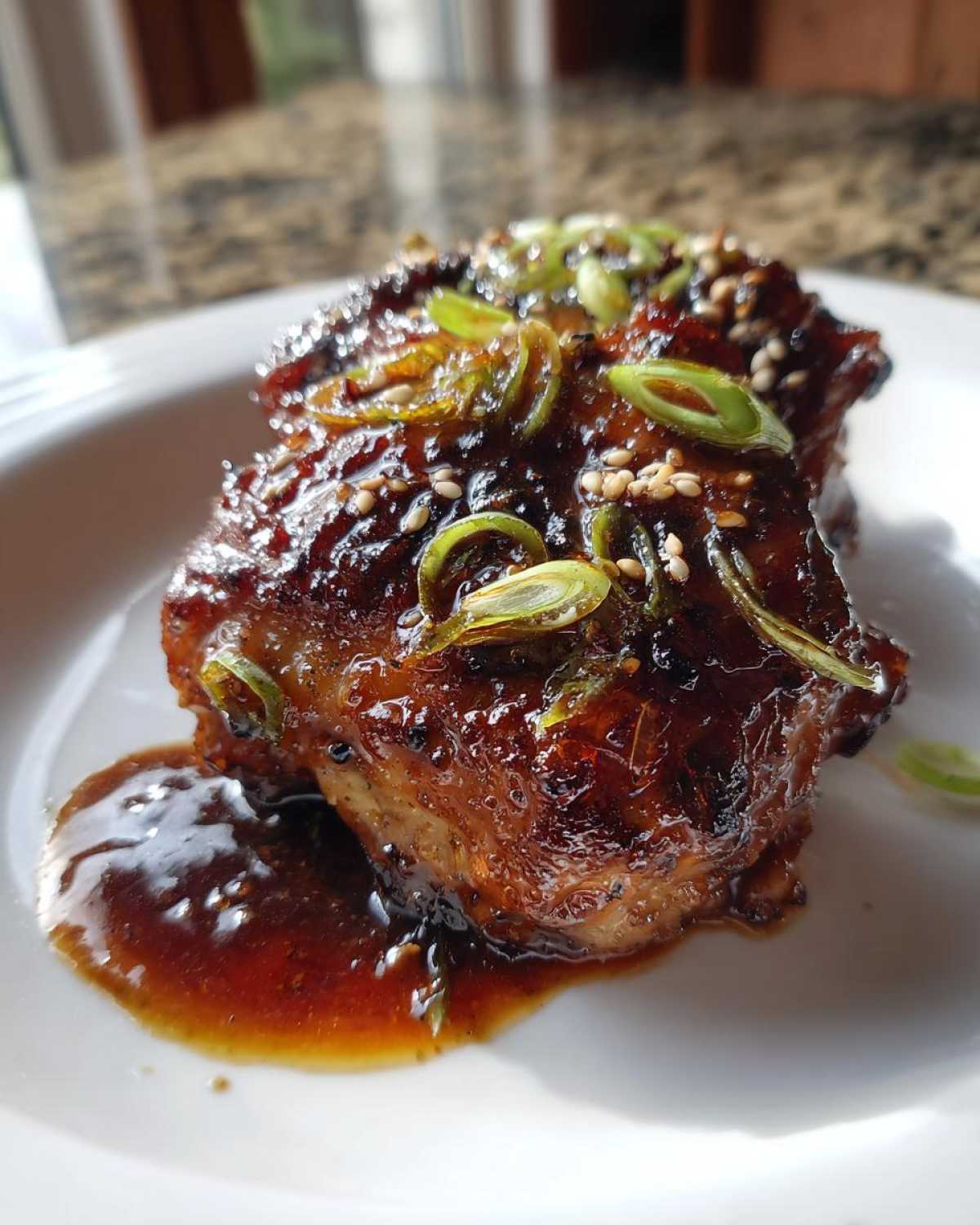 Close-up of glazed Sticky Teriyaki Chicken Thighs with Garlic, topped with sesame seeds and green onions.