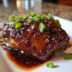 Close-up of a Sticky Teriyaki Chicken Thighs coated in a thick, glossy sauce and topped with sesame seeds and green onions.