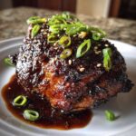 Close-up of a perfectly glazed Sticky Teriyaki Chicken Thighs piece covered in dark sauce, sesame seeds, and sliced green onions.